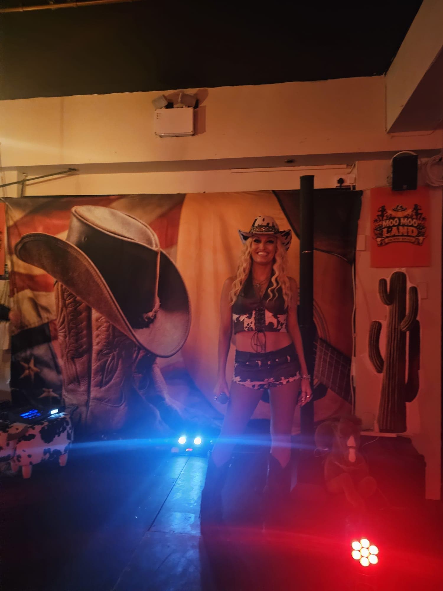 Performer in western dress in front of a cowboy boots backdrop and Moo Moo Land poster at Gracy's